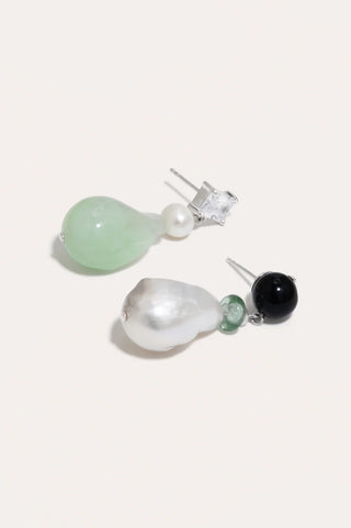 Statement earrings with bold asymmetry, combining pearls, resin, and glass for an elegant look.