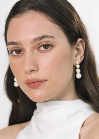 Close-up of a woman wearing pearl earrings against a white background