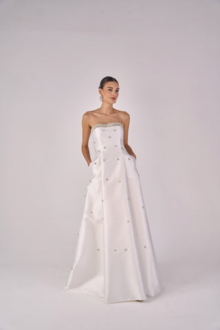 Woman wearing a strapless white gown with buttons on a plain background