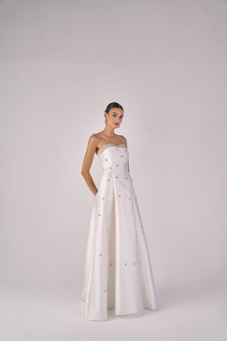 Woman wearing a strapless white gown with floral details on a plain background