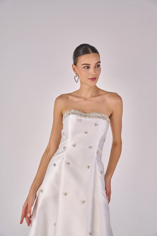 Woman wearing a strapless white wedding dress with bead details on a plain background