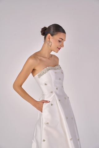 Woman wearing a white saree with silver embellishments on a plain background