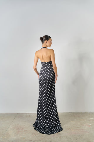 Woman wearing a black and white polka dot halter neck gown against a plain background