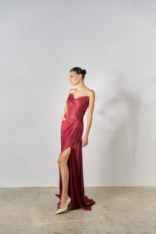 Woman wearing a burgundy evening gown with a slit on a plain background