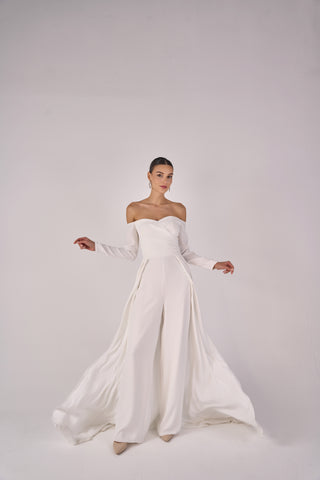 Woman wearing a white strapless jumpsuit with long sleeves on a plain background