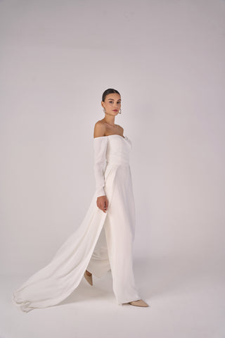 Woman wearing a white off-shoulder jumpsuit on a plain background