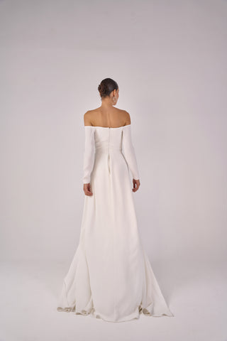 Woman wearing a white off-shoulder long-sleeve wedding jumpsuit on a plain background