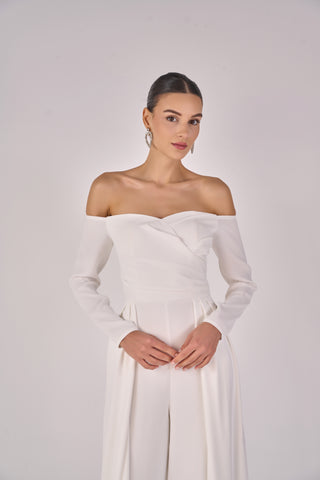 Woman wearing a white off-shoulder jumpsuit against a plain background