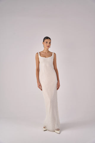 Woman wearing a long, elegant white dress against a plain background