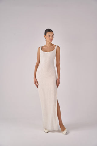 Woman wearing a long, sleeveless cream dress with a slit on a white background