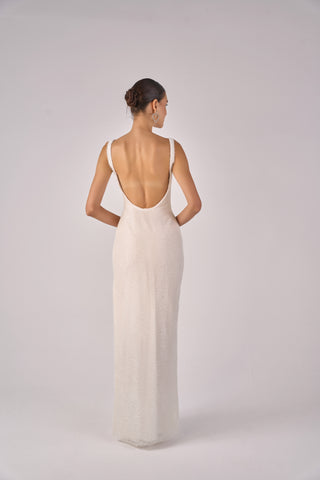 Woman wearing a long, flowing white dress with an open back on a plain background