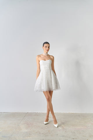 Woman wearing a strapless white dress against a plain background