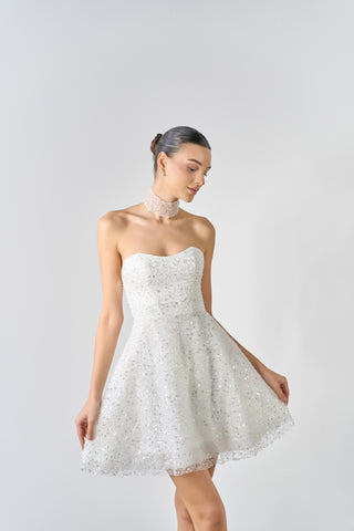 Woman wearing a white strapless dress with lace details on a light gray background