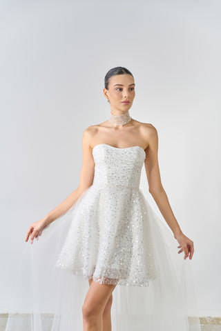 Woman wearing a strapless white lace dress against a plain background