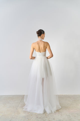 Woman wearing a white strapless gown with a high slit on a plain background