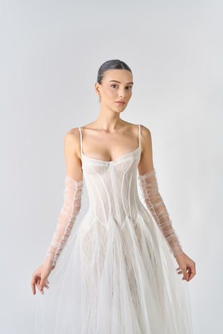 Woman wearing a white wedding dress with sheer sleeves against a light gray background