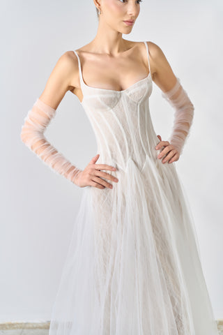 Woman wearing a white wedding dress with sheer gloves against a plain background