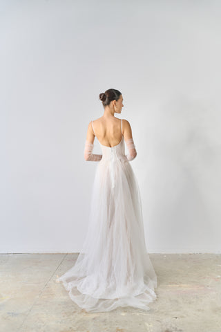 Woman in a white wedding dress standing against a plain white wall.