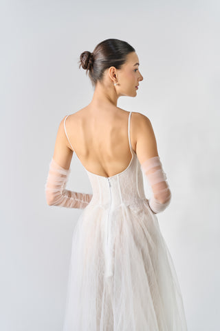 Woman wearing a white wedding dress with sheer sleeves against a light gray background