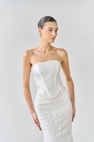 Woman wearing a strapless white wedding dress against a plain background