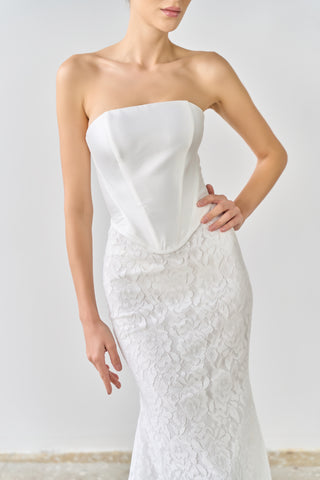 White strapless wedding dress with lace details on a plain background