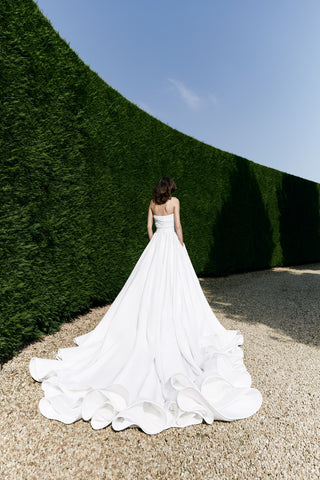 Modern wedding dress showcasing a softly draped bodice, flattering waistline, and bold circular train for a dramatic finish.