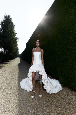 High-low wedding dress with a sleek straight neckline, bustled ruffle accents, and a dramatic flowing train.