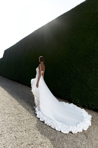 Modern Mikado gown with a structured high-low design, bold bustled hemline, and a sweeping train for bridal elegance.