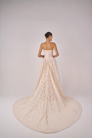 Woman wearing a strapless lace wedding dress with a long train on a plain background