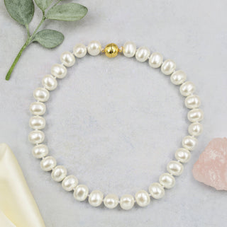 Pearl bracelet with a gold clasp on a light gray background