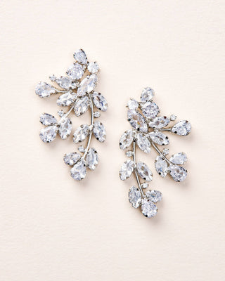 Pair of silver earrings with clear gemstones on a light beige background