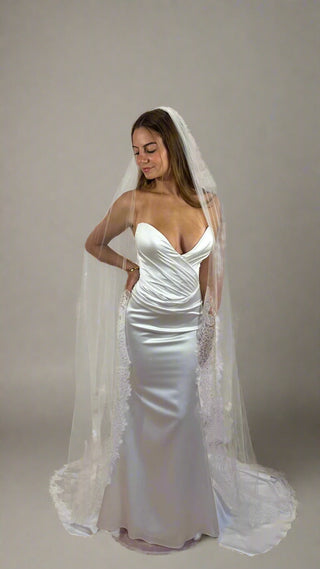 Woman wearing a white wedding dress with a long veil against a plain background