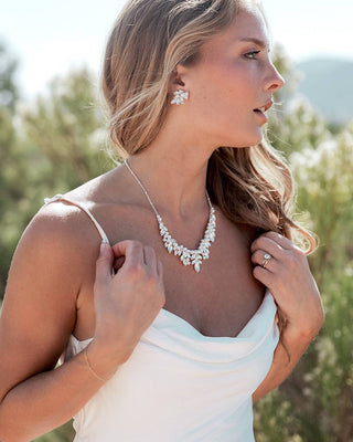 Woman wearing a white dress with a necklace and earrings outdoors