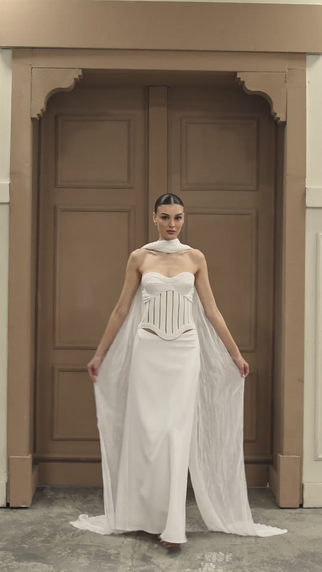 Elegant bridal dress with a structured corset bodice, dramatic scarf accents, and a sleek column silhouette.