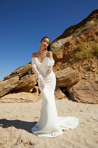 Luxury mermaid bridal gown featuring corseted waist and elegant off-shoulder sleeves with a graceful flare at the knee.